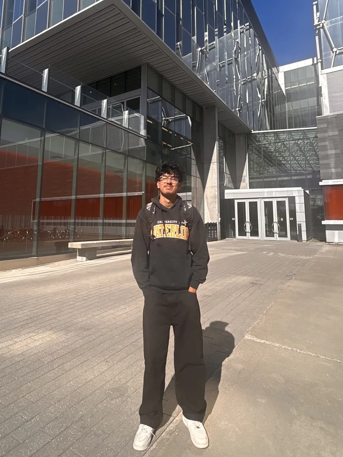 Ahnaf in a University of Waterloo hoodie outside a glass campus building